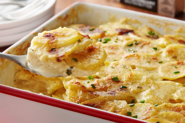 Scalloped potatoes being scooped out of a baking dish