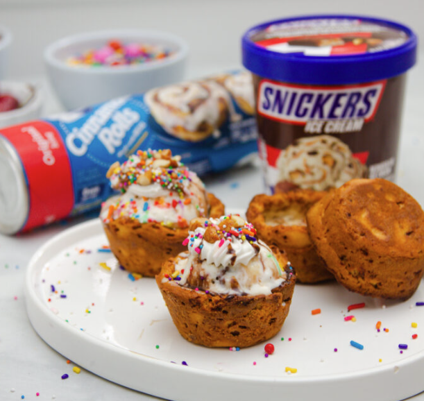 Close up image of cinnamon rolls filled with ice cream and topped with sprinkles on a white plate