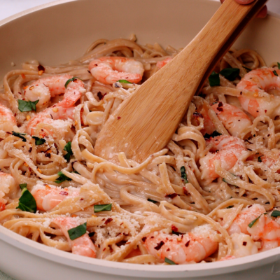 a skillet filled with shrimp alfredo being stirred by a wooden spoon