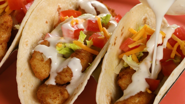 Two tacos side by side, one being drizzled with a creamy sauce