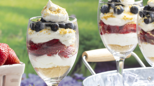 Close up shot of a strawberry and blueberry parfait in a wine glass with grass in the background