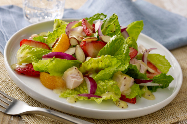 Close up shot of a salad with lettuce, strawberries, almonds, mandarin oranges and red onions all sitting on a white circular plate