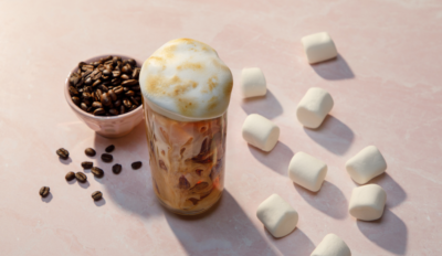 An overhead shot of a glass of toasted marshmallow iced coffee surrounded by marshmallows and a bowl of coffee beans