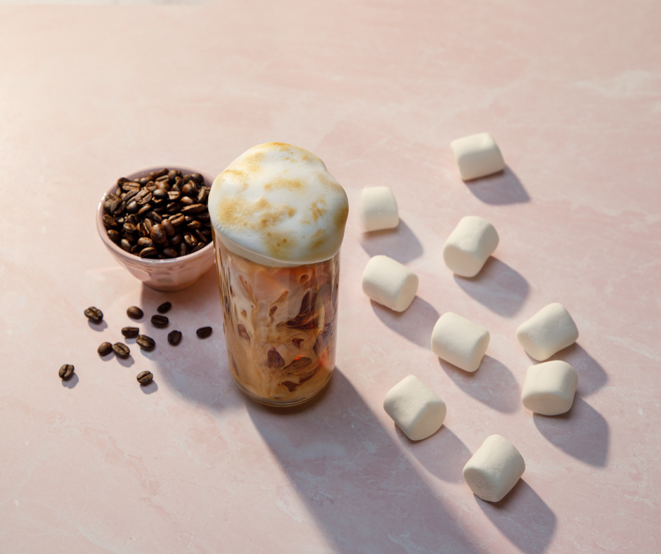 An overhead shot of a glass of toasted marshmallow iced coffee surrounded by marshmallows and a bowl of coffee beans