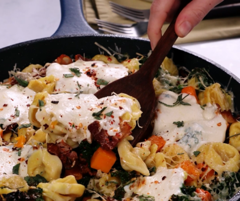 A hand scooping from a tortellini skillet