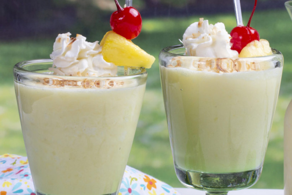 Two glass cups filled with a tropical mother's day drink with whipped cream, pineapple, and cherry on top