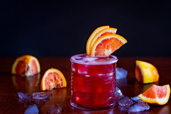 direct shot of a cocktail glass filled with red juice and garnished with blood orange slices surrounded by ice and blood orange slices