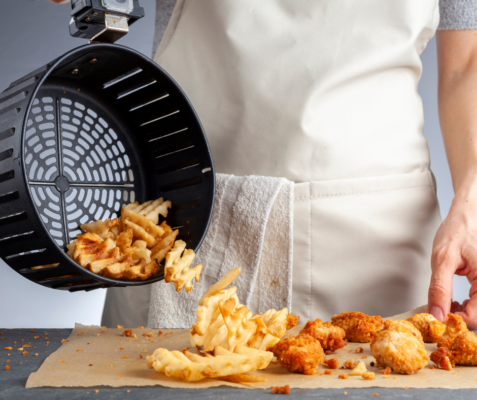 person pouring out food from an air fryer basket onto the counter
