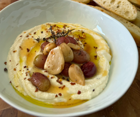 a bowl of whipped ricotta topped with roasted grapes and confit garlic