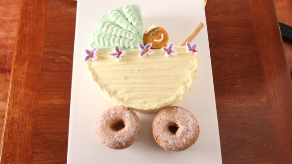 Wooden table with a white plate on top that has a baby shower cake on it and looks like a baby in a stroller