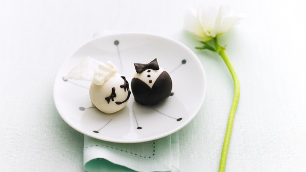 White plate with cookie balls on top, one that looks like a bride and the other that looks like a mens tuxedo