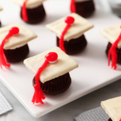Chocolate cupcakes upside down with mini white graduation caps on top sitting on a white plate