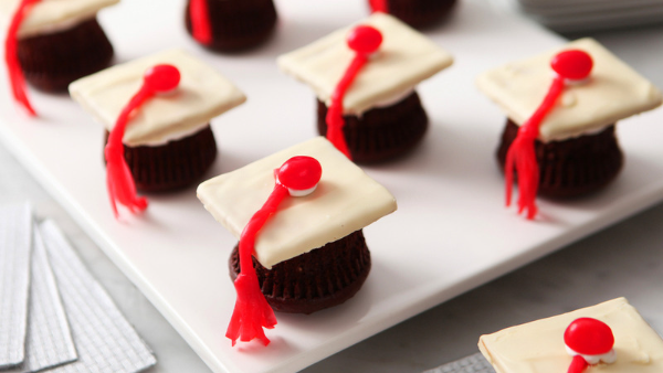 Chocolate cupcakes upside down with mini white graduation caps on top sitting on a white plate