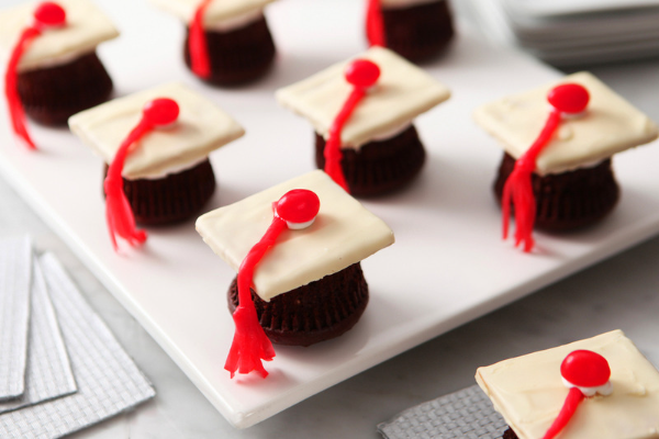 Chocolate cupcakes upside down with mini white graduation caps on top sitting on a white plate