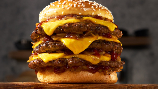 Triple Cheese Burger with Sesame Bun On top of a wood cutting board