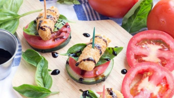 Two Mozzarella Caprese Bites sitting on a wooden cutting board surrounded by basil and tomatoes