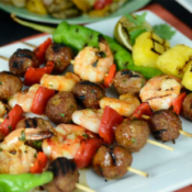 Skewers with meatballs, shrimp, and red peppers laying next to each other on a white plate