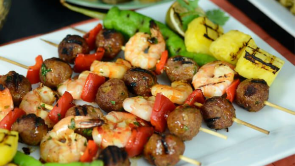 Skewers with meatballs, shrimp, and red peppers laying next to each other on a white plate