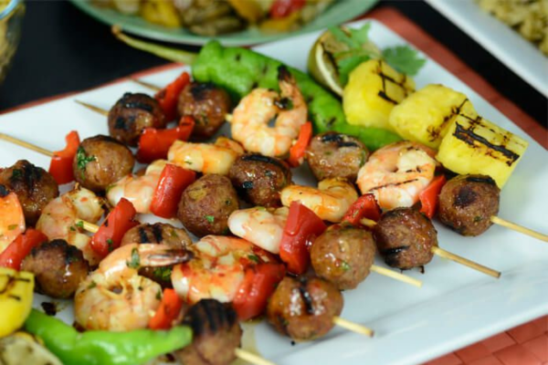 Skewers with meatballs, shrimp, and red peppers laying next to each other on a white plate