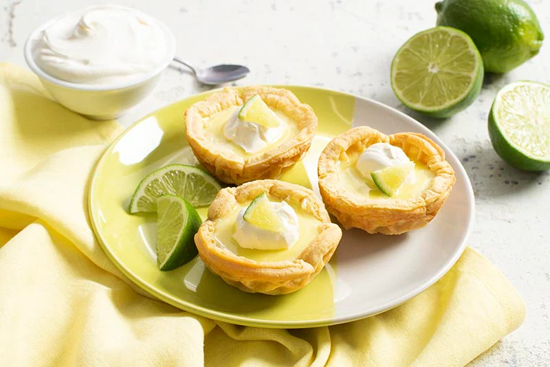 3 Key Lime Tartlets on a white place garnished with limes
