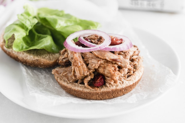 two pieces of bread, one wit pulled pork and onions on top and the other topped with lettuce