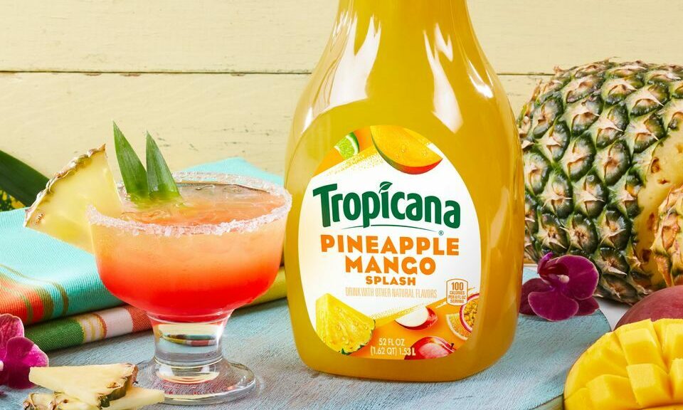 A cocktail in a glass next to a bottle of tropicana pineapple mango juice